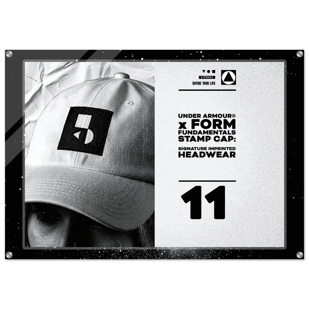 A framed black-and-white promotional print featuring a close-up of a person wearing a baseball cap with a large Under Armour stamp logo. The right side includes text reading 'UNDER ARMOUR x FORM FUNDAMENTAL STAMP CAP: SIGNATURE IMPRINTED HEADWEAR' and the number 11.