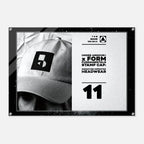 A rectangular black-framed print or poster on a light gray background. The artwork shows a black-and-white close-up of a baseball cap with a square Under Armour logo patch, alongside white text reading 'UNDER ARMOUR x FORM FUNDAMENTALS STAMP CAP' and the number '11'.