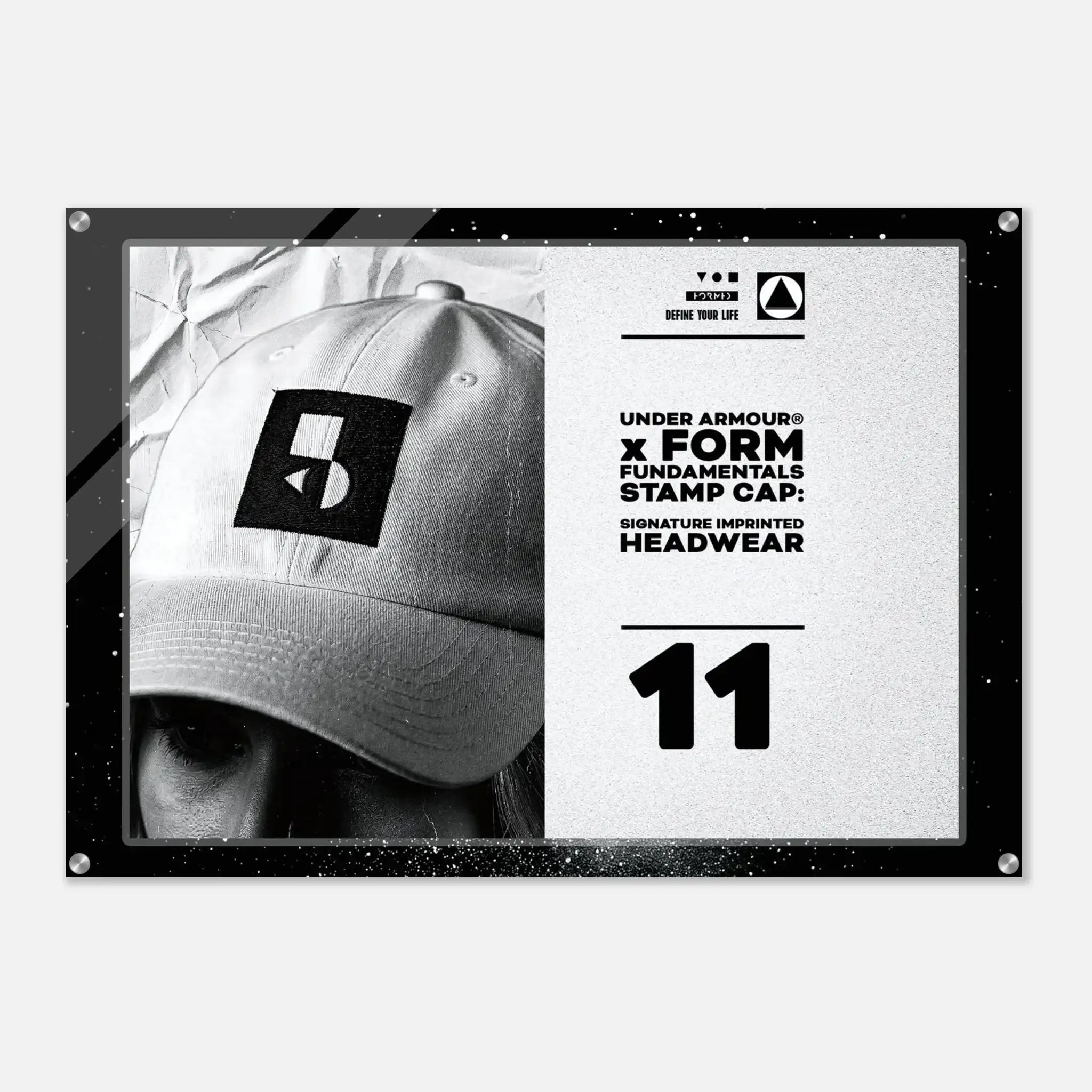 A rectangular black-framed print or poster on a light gray background. The artwork shows a black-and-white close-up of a baseball cap with a square Under Armour logo patch, alongside white text reading 'UNDER ARMOUR x FORM FUNDAMENTALS STAMP CAP' and the number '11'.