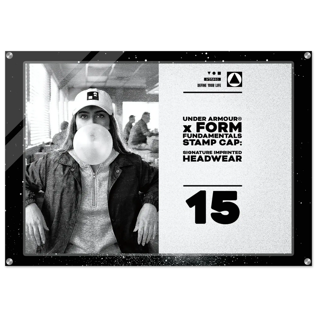 A square promotional display plaque or poster featuring a black-and-white photo of a woman wearing an Under Armour cap and blowing bubble gum, alongside printed text reading 'UNDER ARMOUR x FORM FUNDAMENTALS STAMP CAP: SIGNATURE IMPRINTED HEADWEAR' and the number '15'.