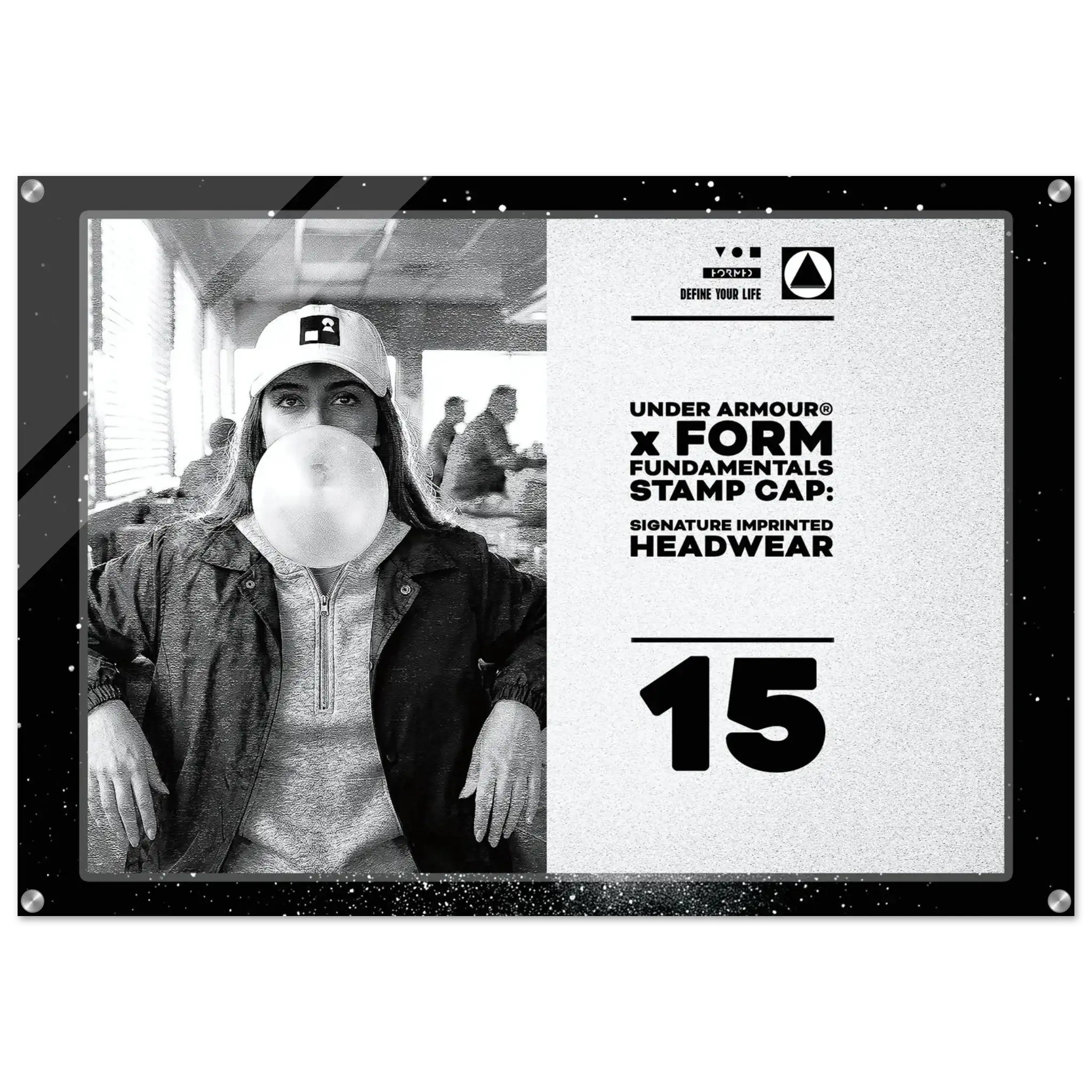 A square promotional display plaque or poster featuring a black-and-white photo of a woman wearing an Under Armour cap and blowing bubble gum, alongside printed text reading 'UNDER ARMOUR x FORM FUNDAMENTALS STAMP CAP: SIGNATURE IMPRINTED HEADWEAR' and the number '15'.
