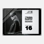 A rectangular acrylic wall art print featuring a black-and-white portrait of a woman wearing a baseball cap on the left, with text on the right that reads 'UNDER ARMOUR x FORM FUNDAMENTALS STAMP CAP' and 'SIGNATURE IMPRINTED HEADWEAR' above a large '16'. The print is shown against a light gray background with a subtle drop shadow.