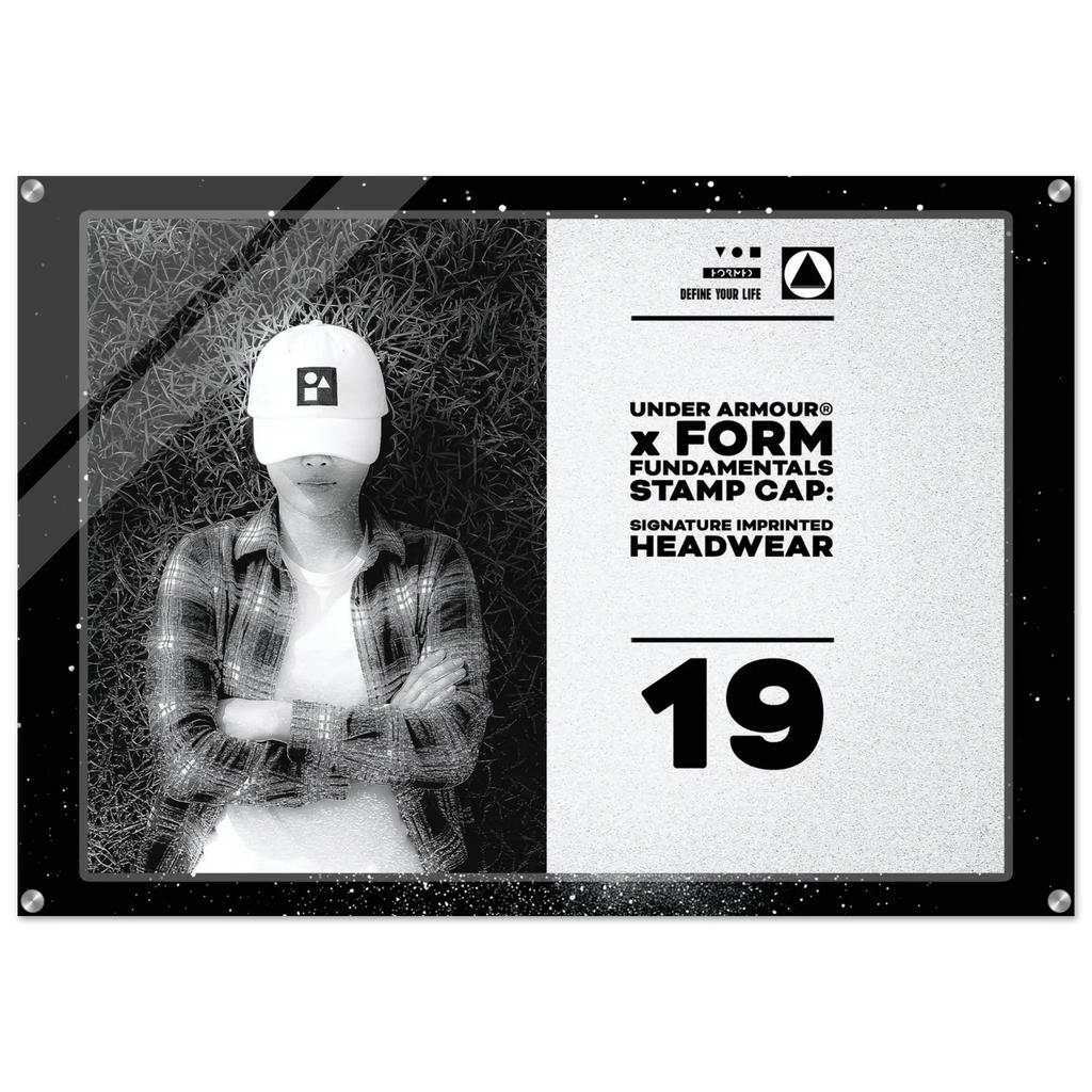 A rectangular acrylic wall art print featuring a black-and-white photo of a person wearing a white Under Armour cap, alongside product text that reads 'UNDER ARMOUR x FORM FUNDAMENTALS STAMP CAP: SIGNATURE IMPRINTED HEADWEAR' and the number '19'.