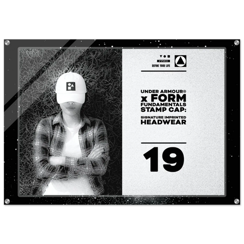 A rectangular acrylic wall art print featuring a black-and-white photo of a person wearing a white Under Armour cap, alongside product text that reads 'UNDER ARMOUR x FORM FUNDAMENTALS STAMP CAP: SIGNATURE IMPRINTED HEADWEAR' and the number '19'.