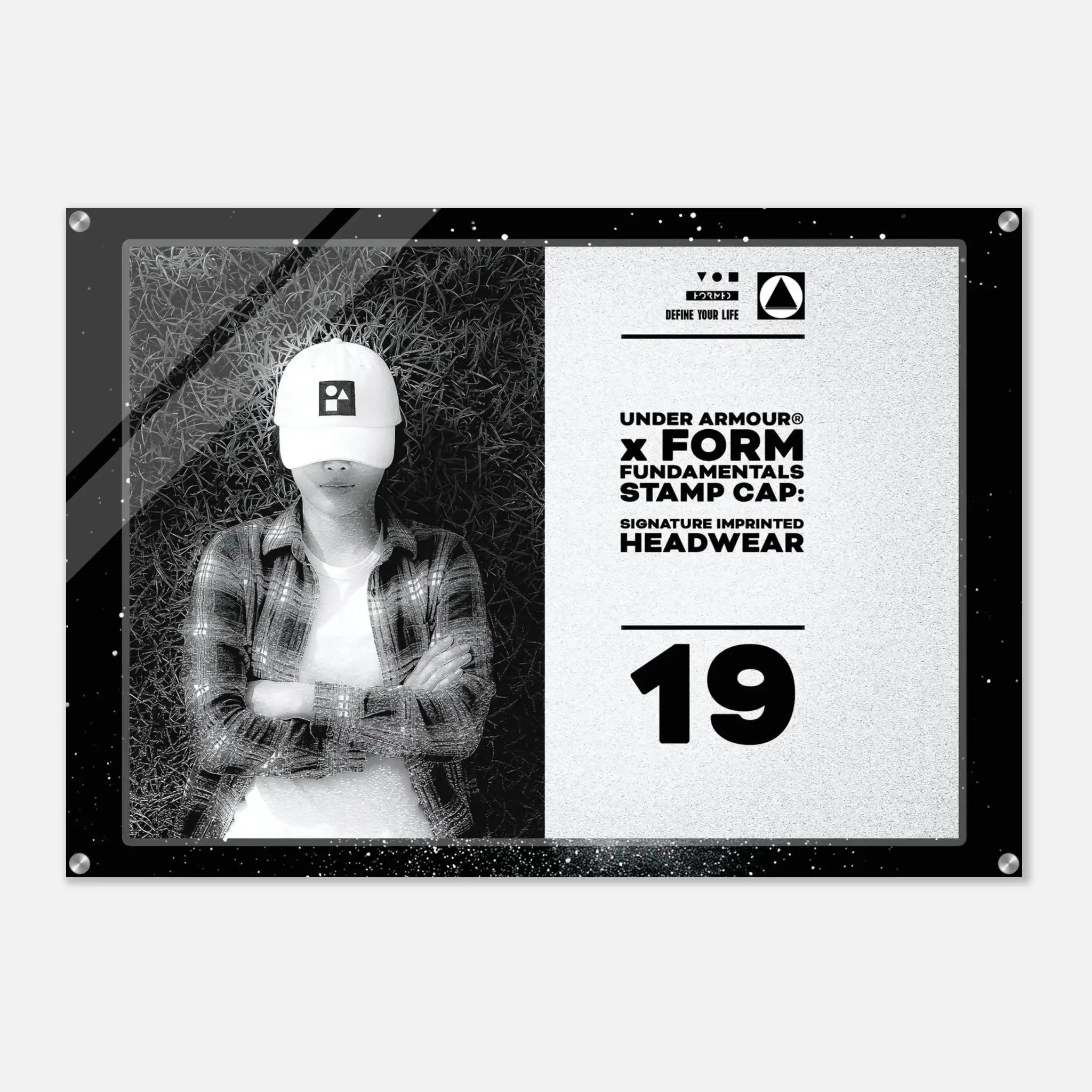 A rectangular acrylic wall art print with a black frame and corner screws, featuring a black-and-white split design. The left side shows a grayscale photo of a person wearing a white cap, and the right side has text reading 'UNDER ARMOUR x FORM FUNDAMENTALS STAMP CAP SIGNATURE IMPRINTED HEADWEAR' with the number 19.