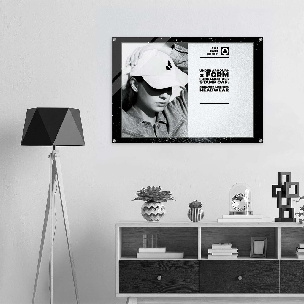 A black-framed poster print hanging on a light gray wall above a white and dark wood media console. The poster features a black-and-white photo of a person wearing a cap and bold text from Form Finding Design.
