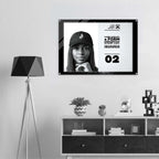A framed black-and-white poster featuring a portrait of a woman in a cap and bold text, displayed on a light wall above a shelf with decor items. A black tripod floor lamp stands to the left.