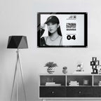 A framed black-and-white promotional print hangs on a light gray wall above a white and dark wood cabinet, next to a black tripod floor lamp. The print shows a woman wearing a baseball cap and includes text from Form Finding Design (FormFD).