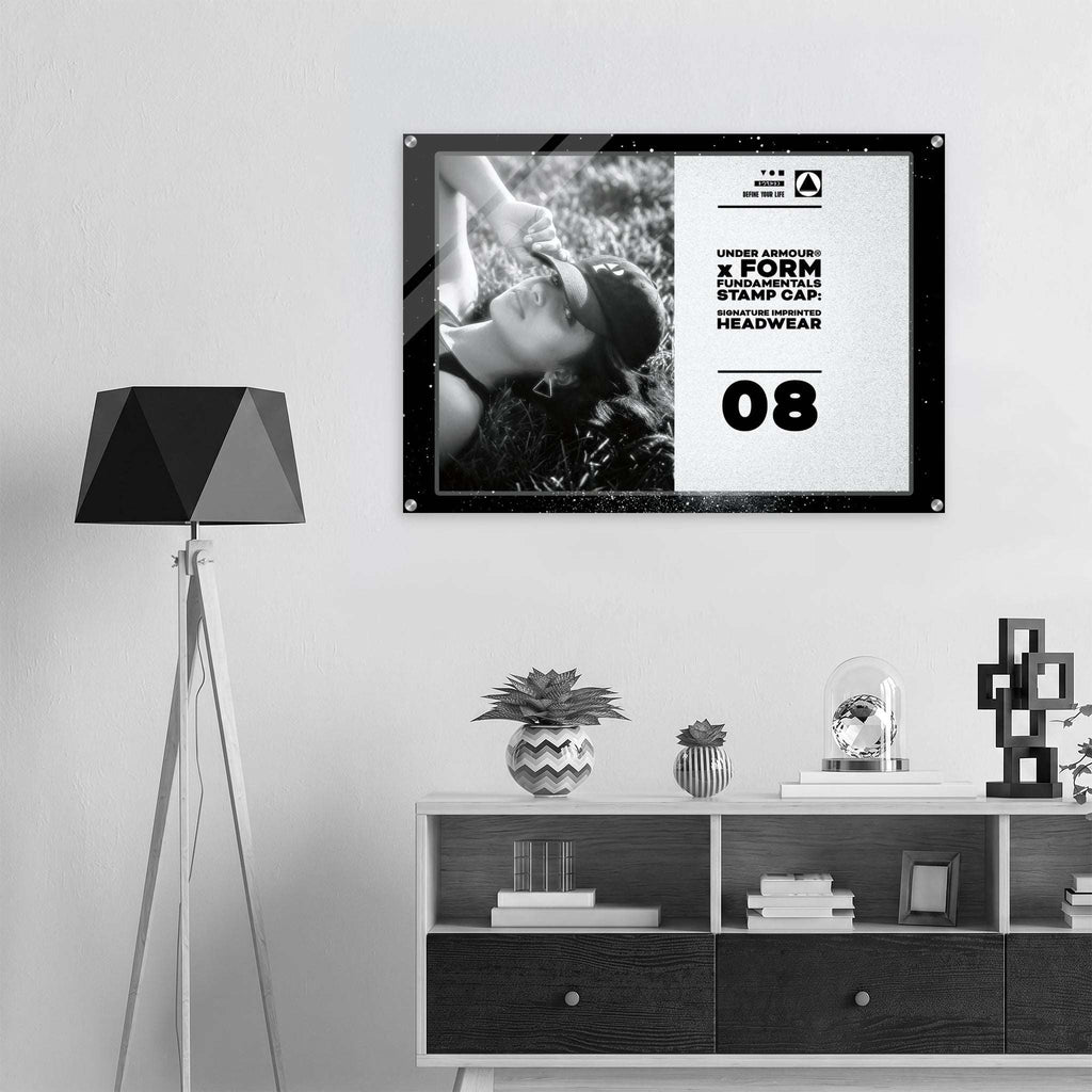 A framed black-and-white poster with bold text and a monochrome photo hangs on a light wall above a shelf in a modern interior setting. The poster includes the text by Form Finding Design.
