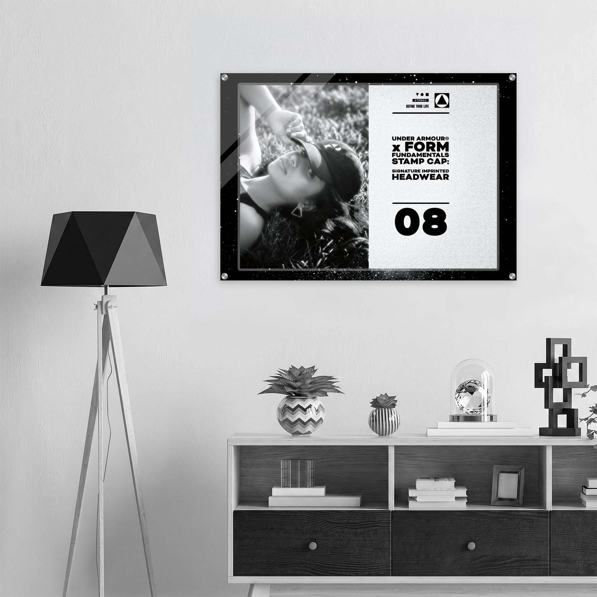 A framed black-and-white poster with bold text and a monochrome photo hangs on a light wall above a shelf in a modern interior setting. The poster includes the text by Form Finding Design.