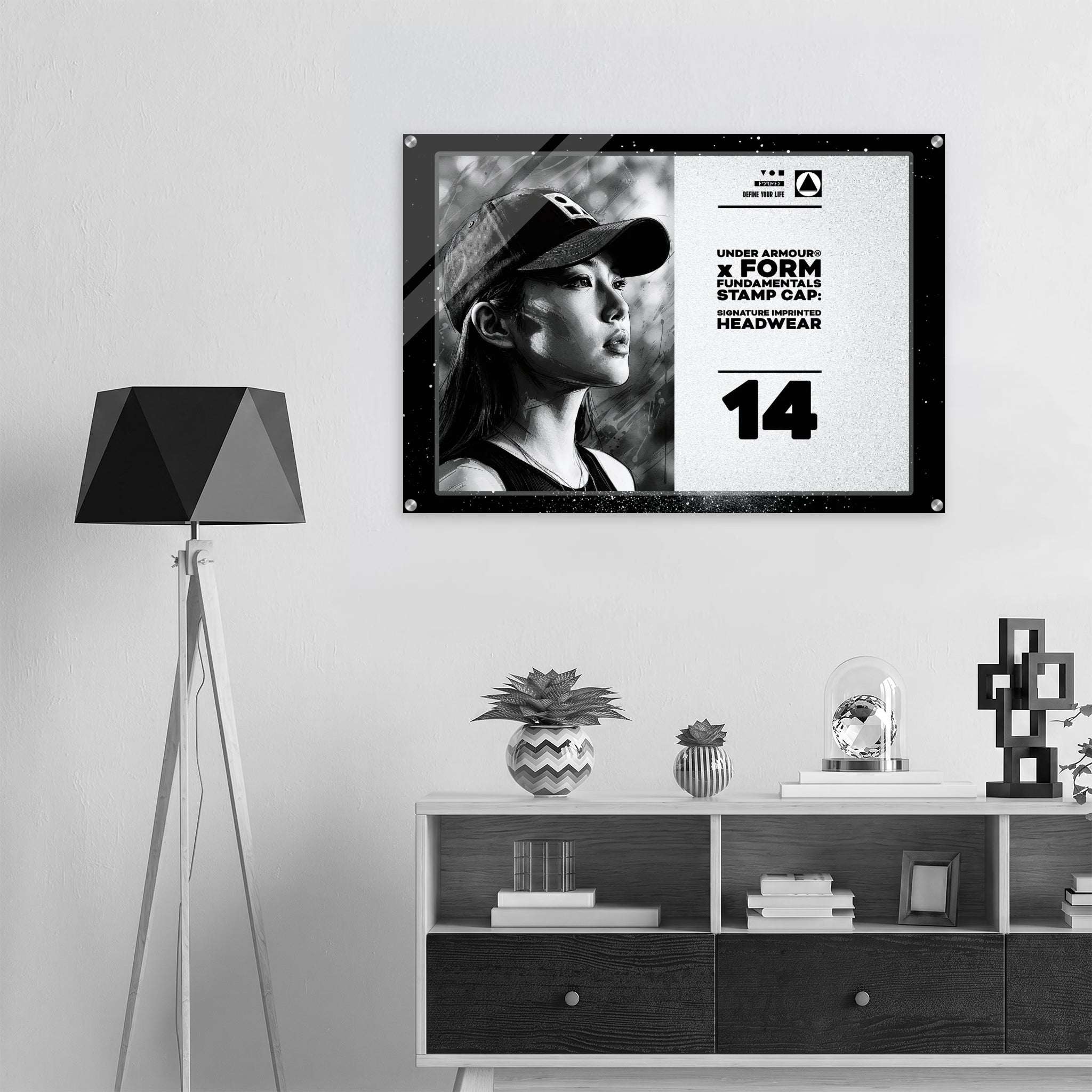 A framed black-and-white poster print hanging on a light gray wall above a white and dark wood cabinet, styled in a modern minimalist room with a black tripod floor lamp and small decor objects.