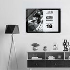 A framed black and white poster hanging on a light gray wall above a white and dark wood shelf, next to a black tripod floor lamp. The poster features a black-and-white photo of a person wearing a cap and the text from Form Finding Design (FormFD).
