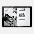 A framed black-and-white promotional print featuring a person wearing a baseball cap with a visible Under Armour stamp, alongside product text reading 'UNDER ARMOUR x FORM FUNDAMENTALS STAMP CAP: SIGNATURE IMPRINTED HEADWEAR.' The print is shown against a light gray background.