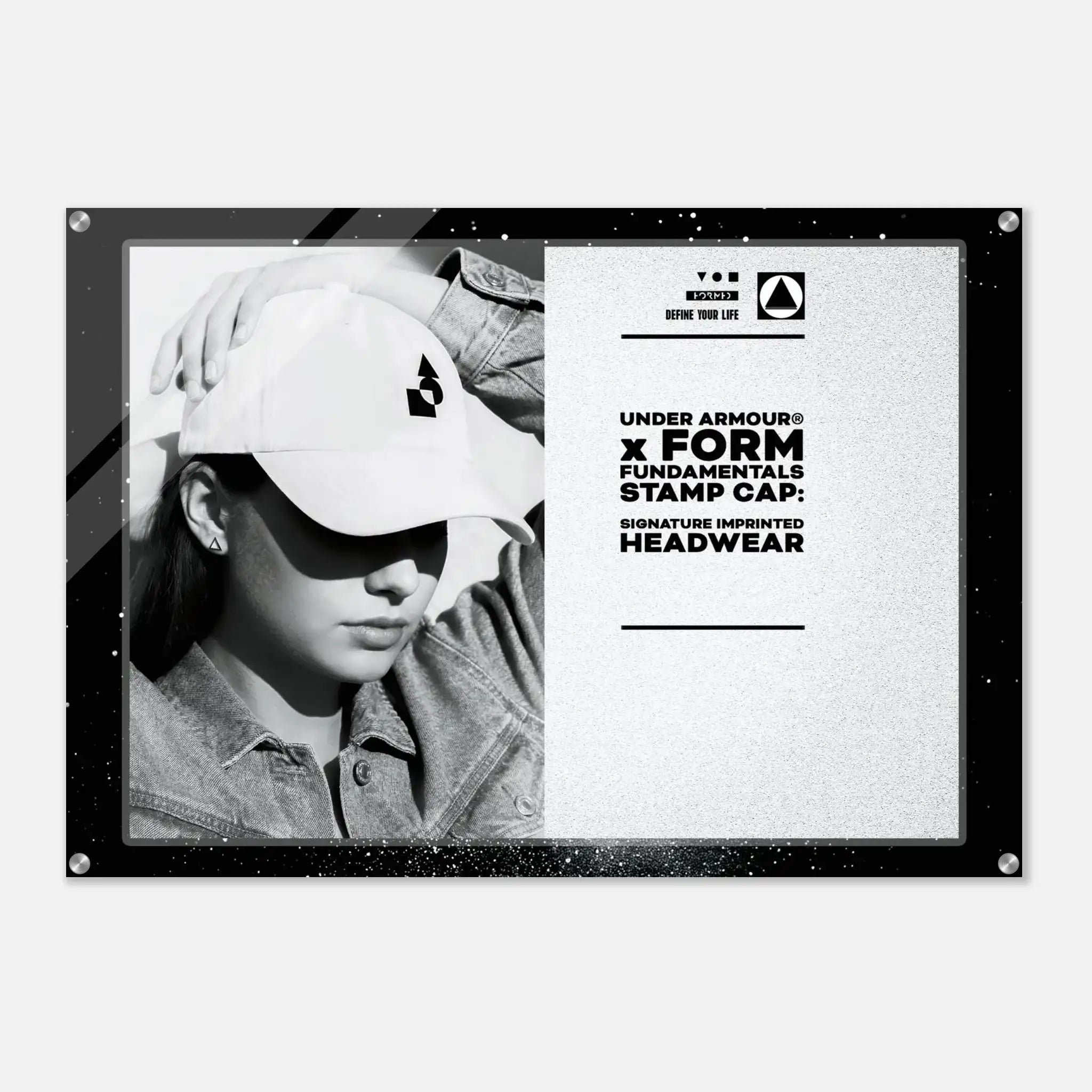 A framed black-and-white promotional print featuring a person wearing a baseball cap with a visible Under Armour stamp, alongside product text reading 'UNDER ARMOUR x FORM FUNDAMENTALS STAMP CAP: SIGNATURE IMPRINTED HEADWEAR.' The print is shown against a light gray background.