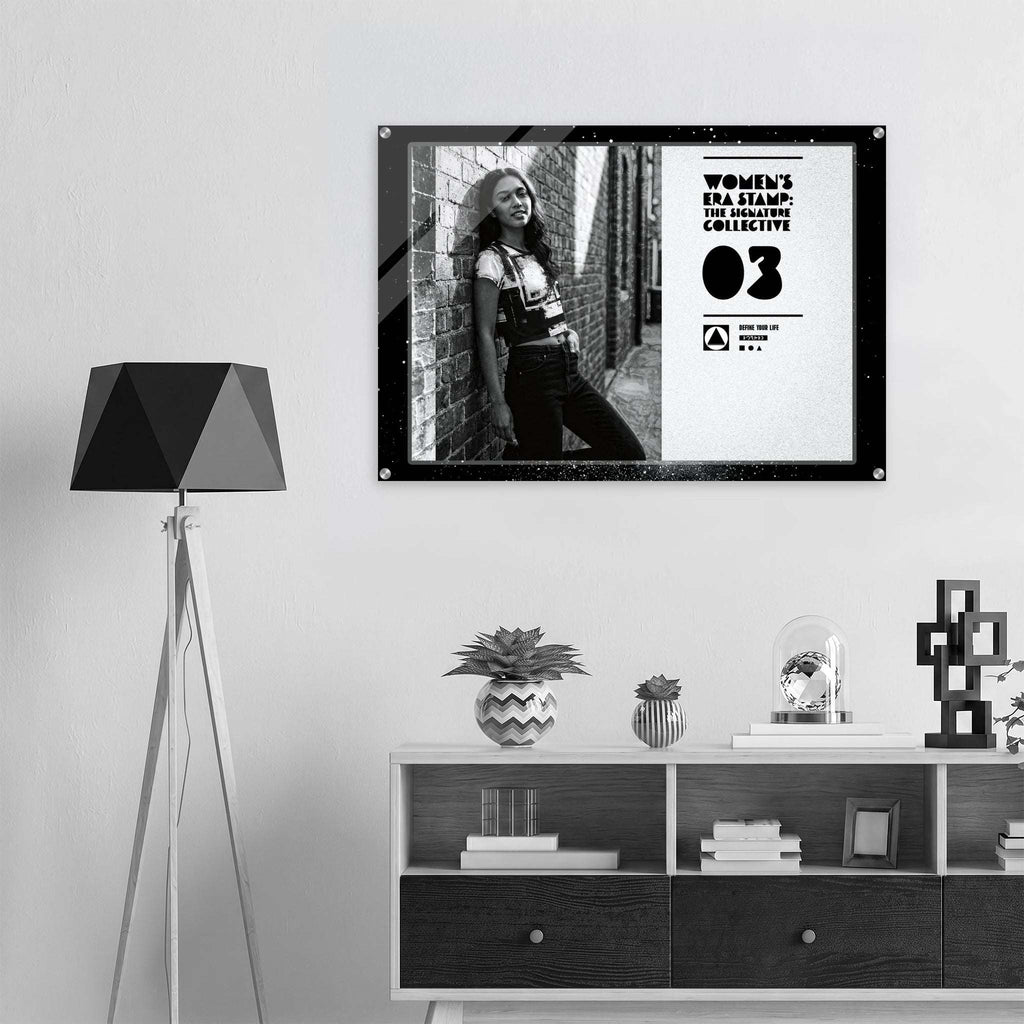 Framed artwork of a woman leaning against a brick wall on a wall above a shelf with decorative items.