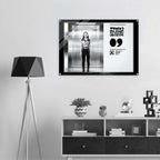 Framed artwork of a woman in an elevator on a wall above a shelf with decorative items.