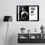 Framed artwork of a woman with a back tattoo displayed on a wall above a shelf.
