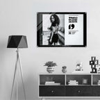 Framed poster of a woman with text on a wall above a shelf with decorative items.