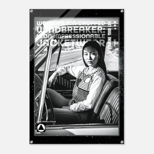 A black and white poster print featuring a woman sitting in a car interior, with bold text overlays including 'WOMEN'S ICON CROPPED WINDBREAKER: ICON IMPRESSIONABLE JACKETWEAR' and 'DEFINE YOUR LIFE.' The poster is shown hanging against a light gray wall.