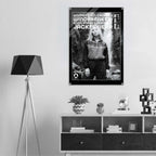 A black and white poster featuring a model hanging on a light gray wall in a modern, minimalist room setting with a tripod floor lamp and a wooden shelf below.