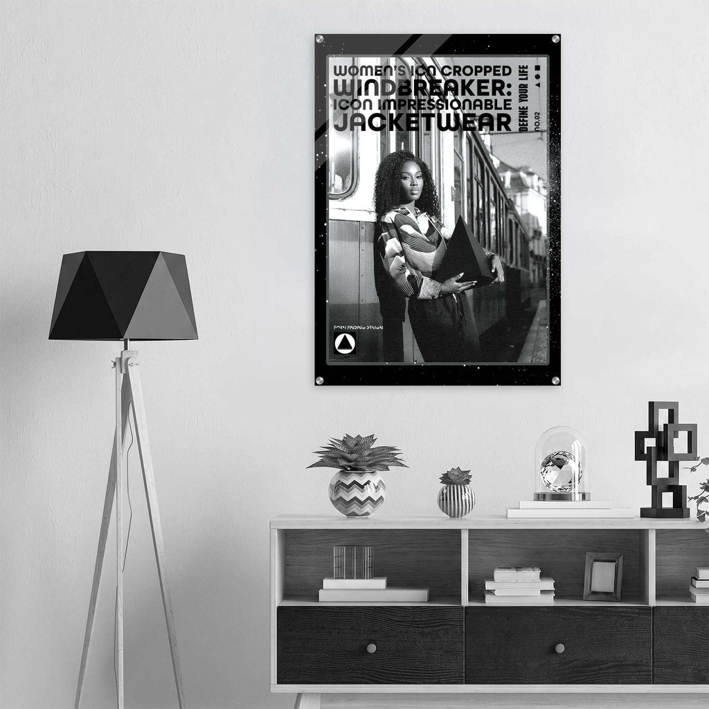 A black and white framed poster hanging on a light gray wall above a modern wooden shelf with decorative items, next to a black tripod floor lamp.