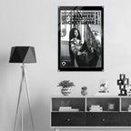 A black and white framed poster hanging on a light gray wall above a modern wooden shelf with decorative items, next to a black tripod floor lamp.