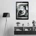 A black and white framed poster featuring a woman in a car with bold text, displayed on a light gray wall above a modern shelf with decorative items and a tripod floor lamp.