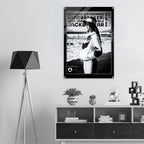 A black and white poster featuring a woman wearing a cap and jacket, with bold text including 'women's icon CROPPED WINDBREAKER: ICON IMPRESSIONABLE JACKETWEAR', displayed on a light gray wall above a shelf in a modern interior setting.