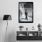 A black and white framed poster featuring a model walking in a street scene with bold text reading 'WOMEN'S ICON CROPPED WINDBREAKER: ICON IMPRESSIONABLE JACKETWEAR', displayed on a light gray wall above a modern shelf in a styled interior setting.
