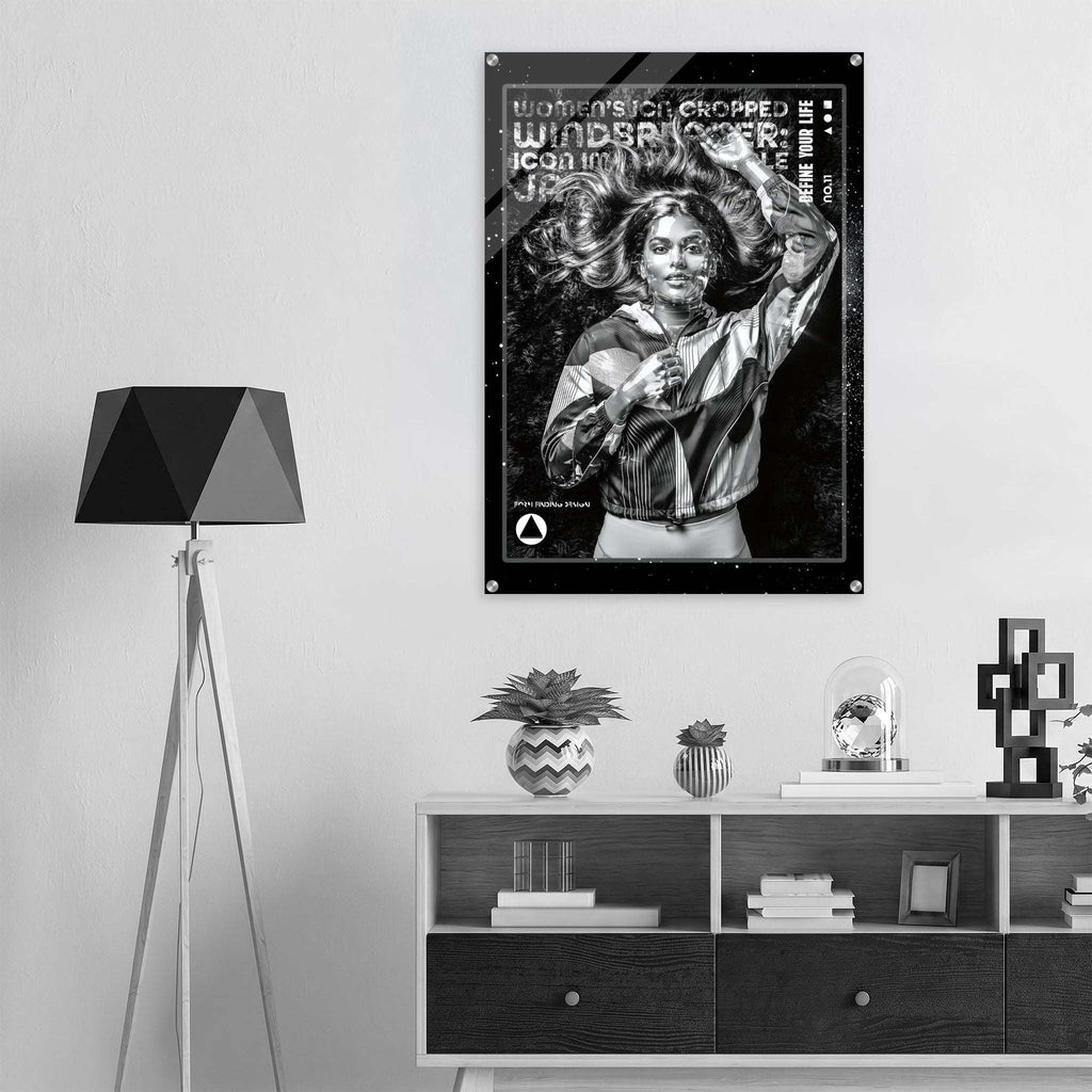 A black and white poster featuring a woman with the text 'WOMEN ICON CROPPED WINDBREAKER' hangs on a light gray wall above a shelf with decor items in a modern room setting.
