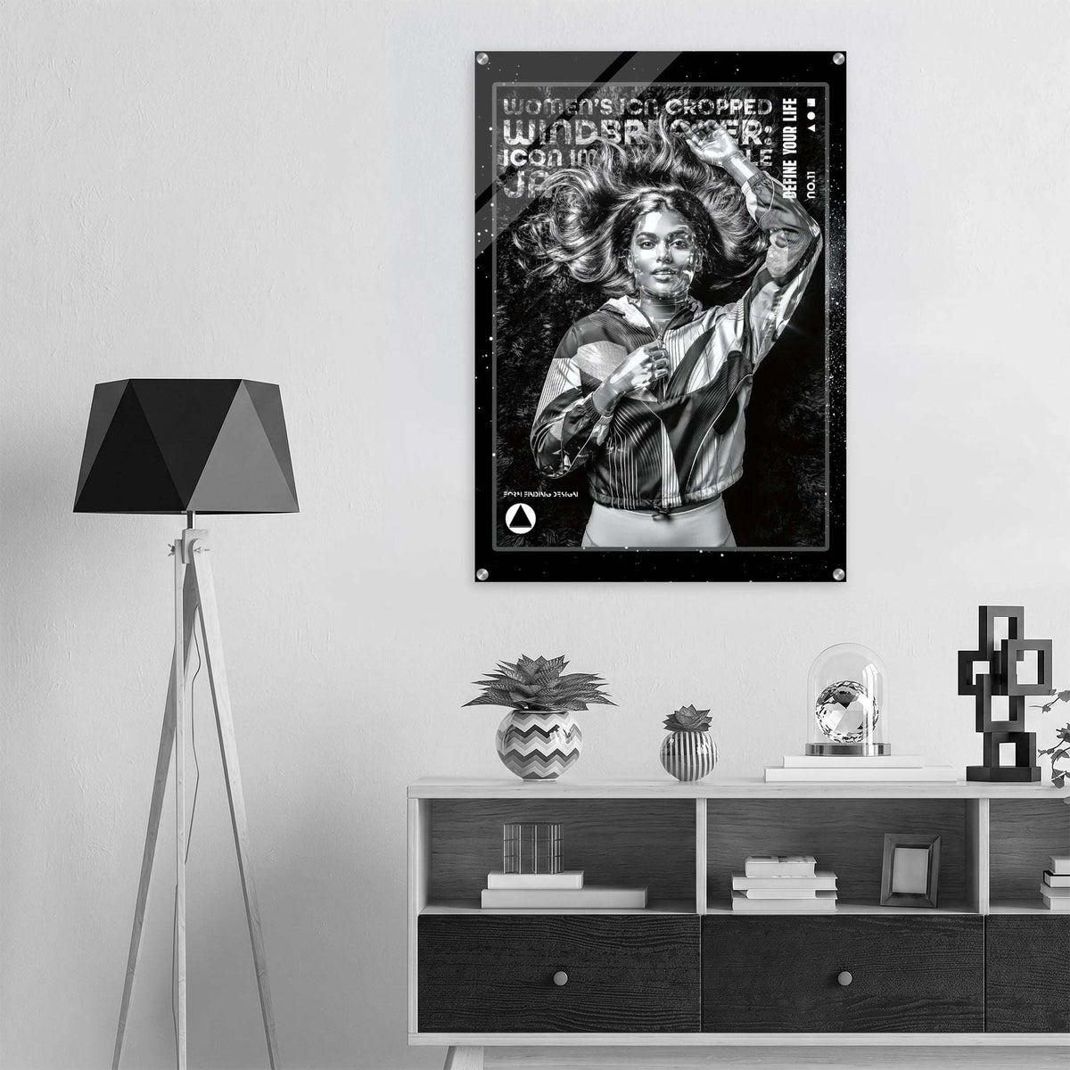 A black and white poster featuring a woman with the text 'WOMEN ICON CROPPED WINDBREAKER' hangs on a light gray wall above a shelf with decor items in a modern room setting.