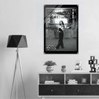 A black and white framed poster of the women's icon cropped windbreaker no.12 displayed on a light gray wall in a modern, minimalist room setting with a tripod floor lamp and a wooden shelf.