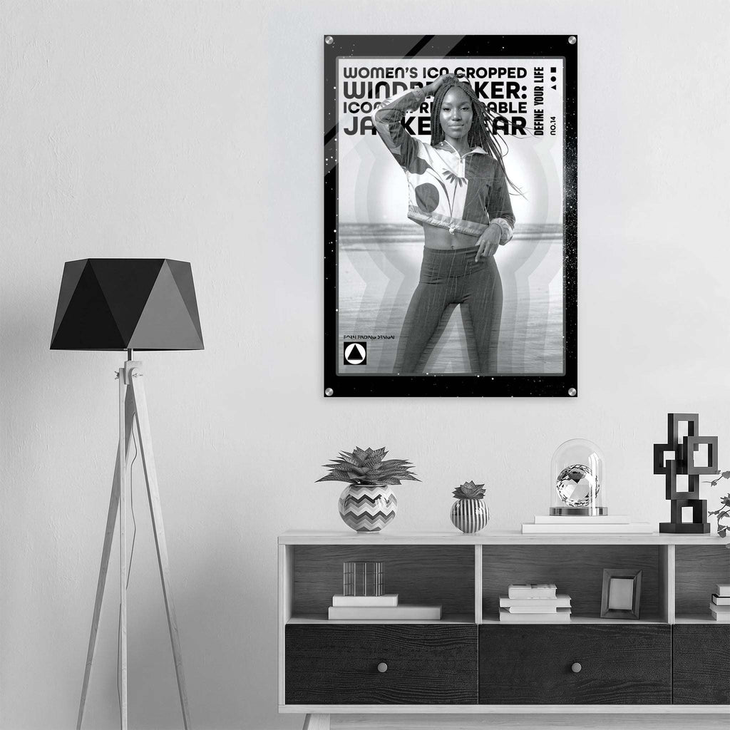 A black and white framed poster hangs on a light gray wall above a modern white and dark wood console table. The room is styled with a black tripod floor lamp on the left, decorative plants, books, and a glass dome.