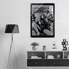 A black and white framed poster hanging on a light gray wall above a wooden shelf, showing a seated woman in athletic wear with bold text reading 'Women's Icon Cropped Windbreaker: Impressionable Jacketwear.' The room includes a black floor lamp on the left and decorative objects on the shelf below.