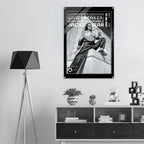 A black and white poster print featuring a woman in a jacket and pants, mounted on a light gray wall above a white shelf with decorative items. The poster text reads 'WOMEN'S ICON CROPPED WINDBREAKER: ICON IMPRESSIONABLE JACKETWEAR'.