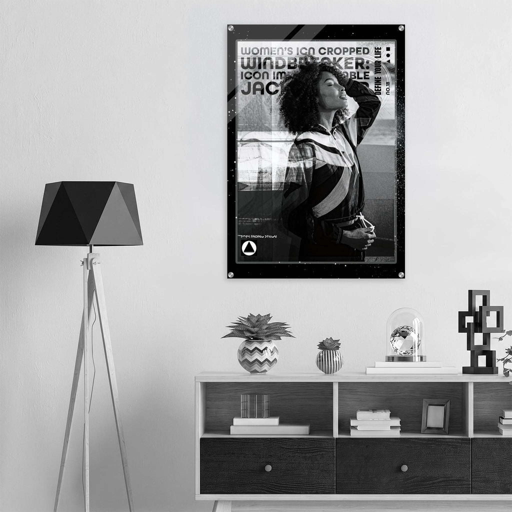 A black and white framed poster featuring a woman and bold text hangs on a light gray wall above a white shelf with decorative objects. A black tripod floor lamp stands to the left.