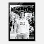 A black-framed poster or print featuring a black-and-white photo of a smiling woman wearing a white hoodie with bold text on the front. The poster includes decorative light streak graphics and text at the top reading 'WOMEN'S SIGNATURE HOODIE IMPRINTED ICONOGRAPHY WEAR'.