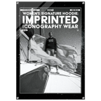 A black rectangular poster or print with rounded corners and visible mounting holes, featuring bold white text reading 'WOMEN'S SIGNATURE HOODIE: IMPRINTED ICONOGRAPHY WEAR' above a black-and-white photo of a person standing on a boat deck with flowing fabric. The product is shown against a light gray background.