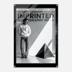 A black and white fashion poster print featuring a model wearing a hoodie and jeans, with bold text reading 'WOMEN'S SIGNATURE HOODIE: IMPRINTED ICONOGRAPHY WEAR' and a black geometric pyramid in the foreground.