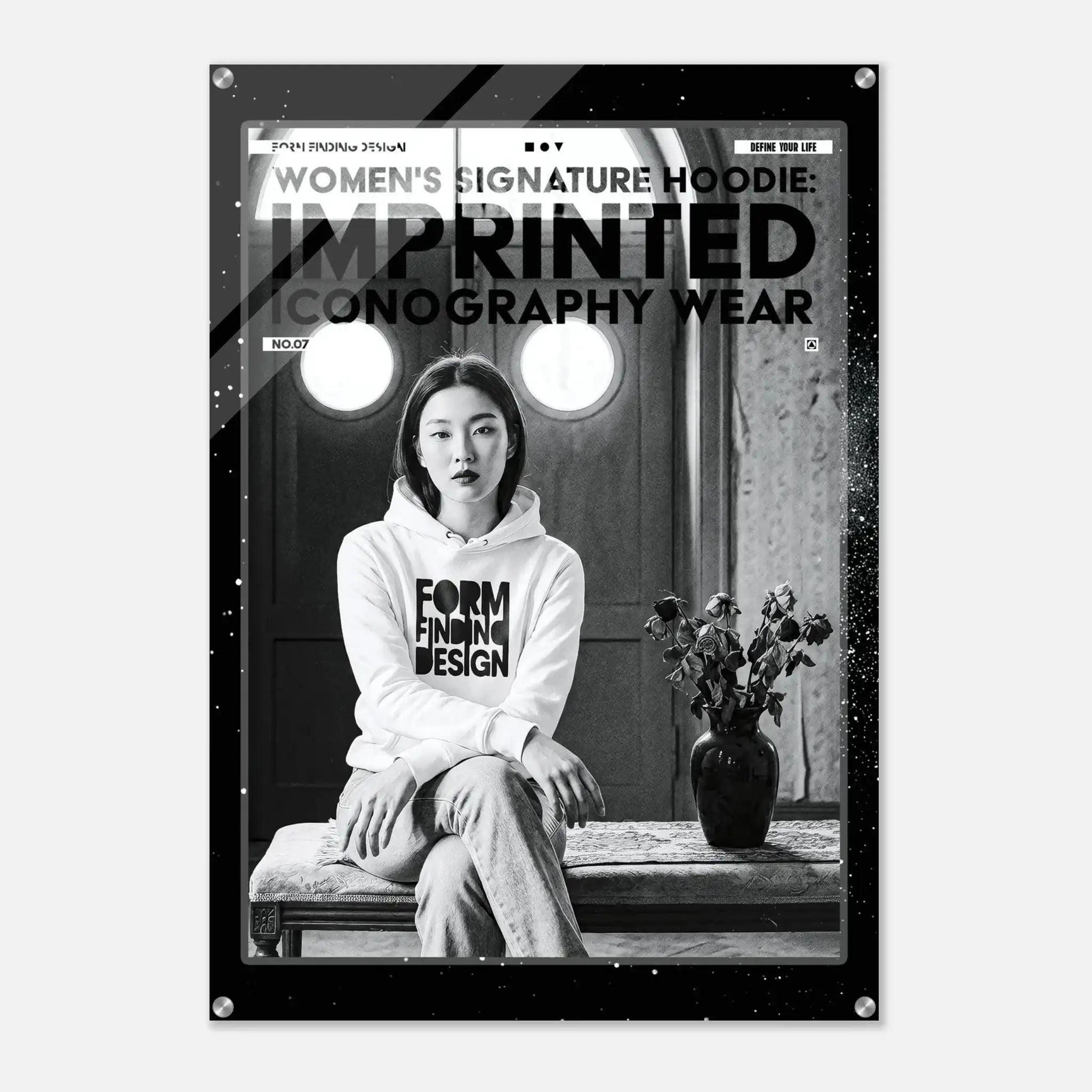 A black and white fashion poster featuring a seated woman in a hoodie with bold text reading 'WOMEN'S SIGNATURE HOODIE: IMPRINTED ICONOGRAPHY WEAR.' The poster is shown hanging against a light gray wall, with visible metal corner hardware.