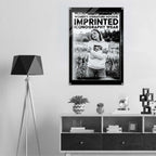 A black and white poster print featuring a woman in a hoodie in a field, with bold text reading 'WOMEN'S SIGNATURE HOODIE IMPRINTED ICONOGRAPHY WEAR', displayed on a wall above a modern console table in a minimalist room setting.