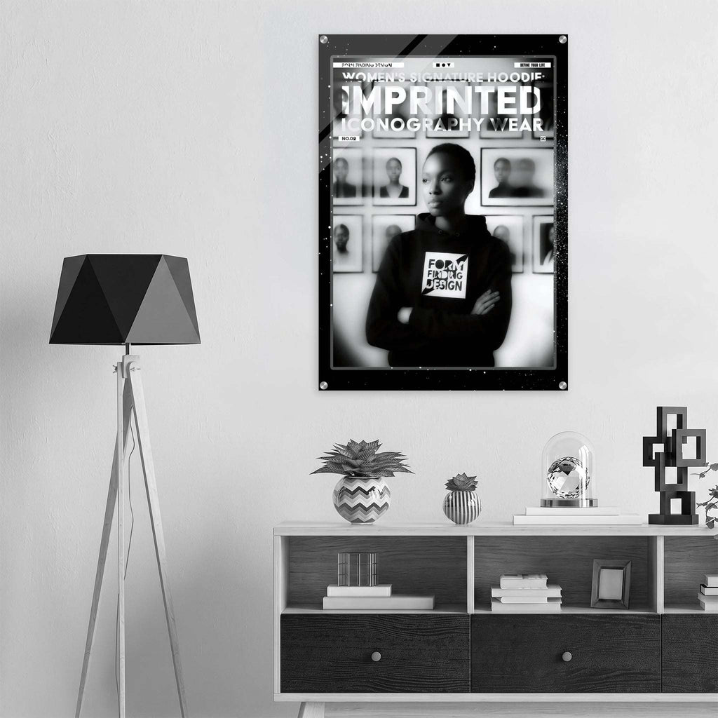A black and white framed poster hanging on a light gray wall above a white shelf with books and decor. The poster features a person wearing a hoodie with the text 'FORM FINDING DESIGN' and the headline 'WOMEN'S SIGNATURE HOODIE IMPRINTED ICONOGRAPHY WEAR'.