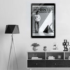 A black-framed wall art print hangs above a white cabinet in a modern room. The print features a black-and-white fashion poster with the text 'WOMEN'S SIGNATURE HOODIE IMPRINTED ICONOGRAPHY WEAR' and a photo of a person wearing a hoodie.