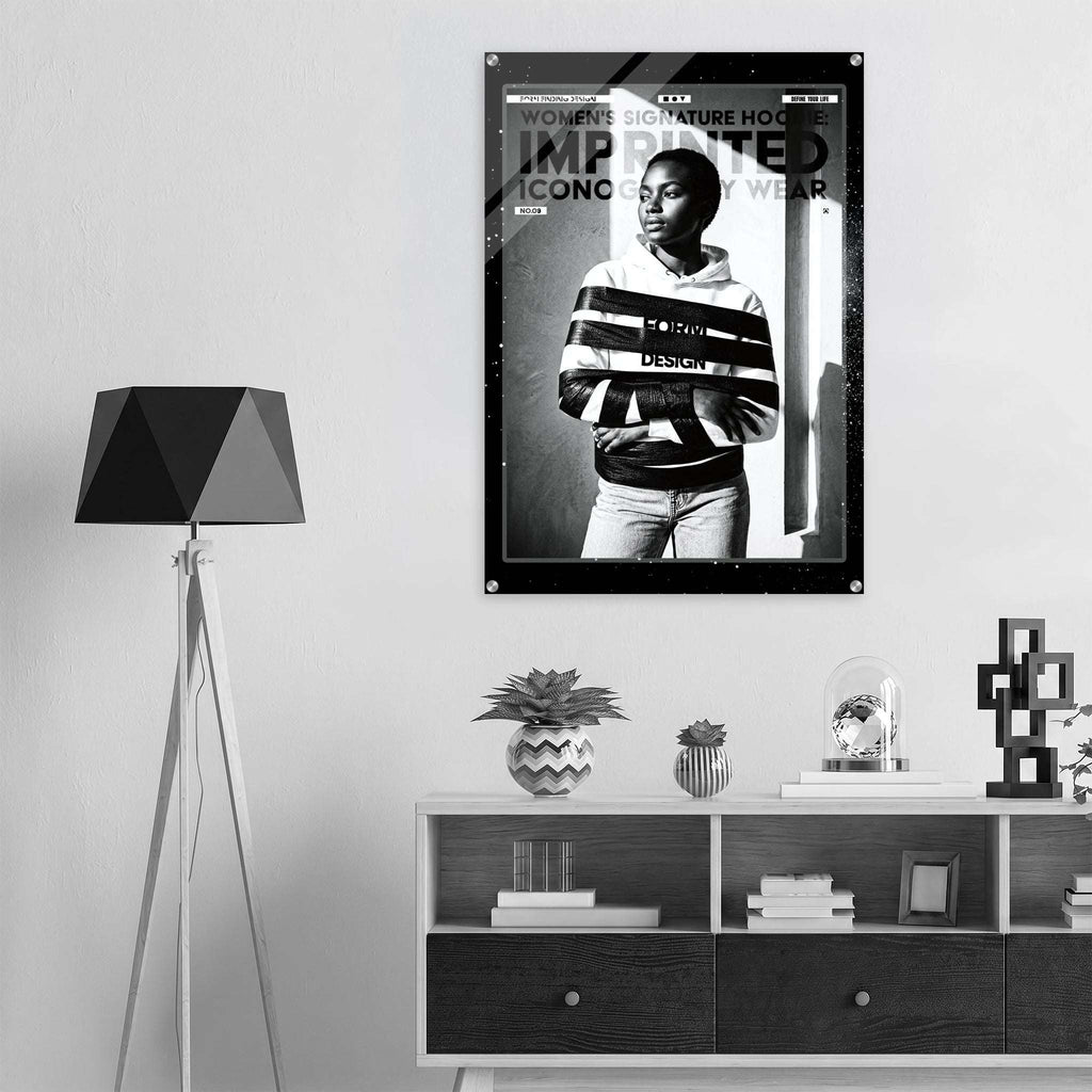 A black and white fashion poster featuring a model in a striped hoodie, displayed on a light gray wall above a modern white and dark wood console shelf with decorative items and a black tripod floor lamp.