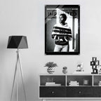 A black and white fashion poster featuring a model in a striped hoodie, displayed on a light gray wall above a modern white and dark wood console shelf with decorative items and a black tripod floor lamp.