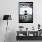 A black and white poster featuring a woman running through grass with the text 'WOMEN'S SIGNATURE HOODIE IMPRINTED ICONOGRAPHY WEAR' and 'FORM FINDING DESIGN', displayed on a wall above a shelf in a modern room setting.