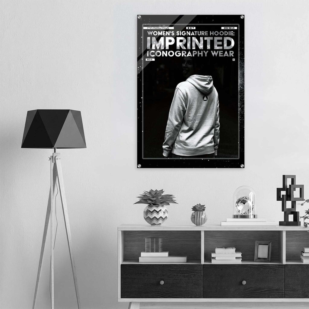 A black and white poster featuring a hoodie iconography design hangs on a light gray wall above a white and dark wood console shelf in a modern room setting.