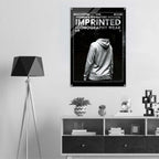 A black and white poster featuring a hoodie iconography design hangs on a light gray wall above a white and dark wood console shelf in a modern room setting.