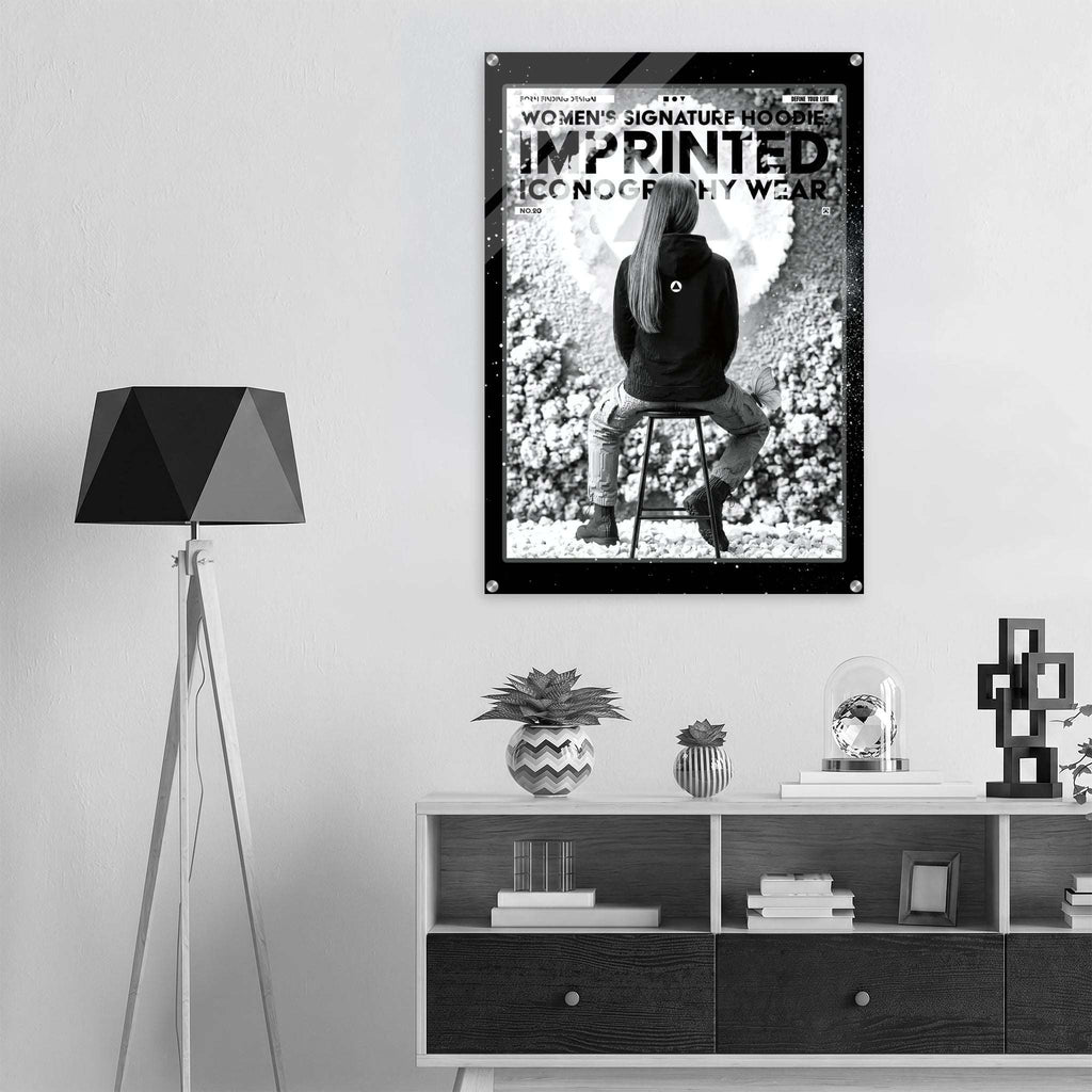 A black and white poster featuring a seated woman with the text 'WOMEN'S SIGNATURE HOODIE IMPRINTED ICONOGRAPHY WEAR.
