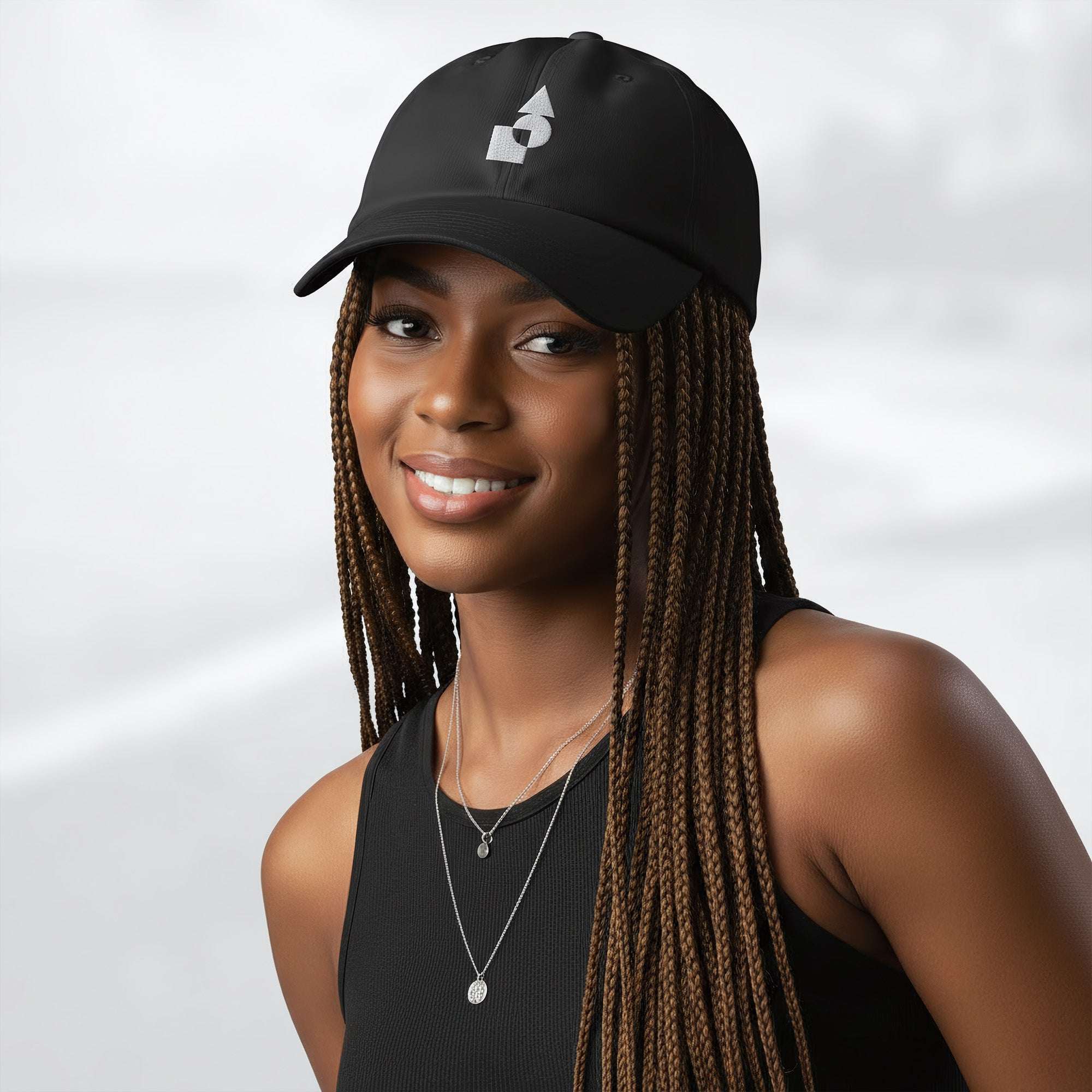 Female model wearing the black Under Armour x Form Fundamentals Stamp Cap (No.02); front view of the cap with white geometric emblem and curved brim, paired with a black tank top and layered necklaces against a softly blurred background.